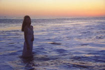 Silhouette of woman standing knee deep in ocean at sunset